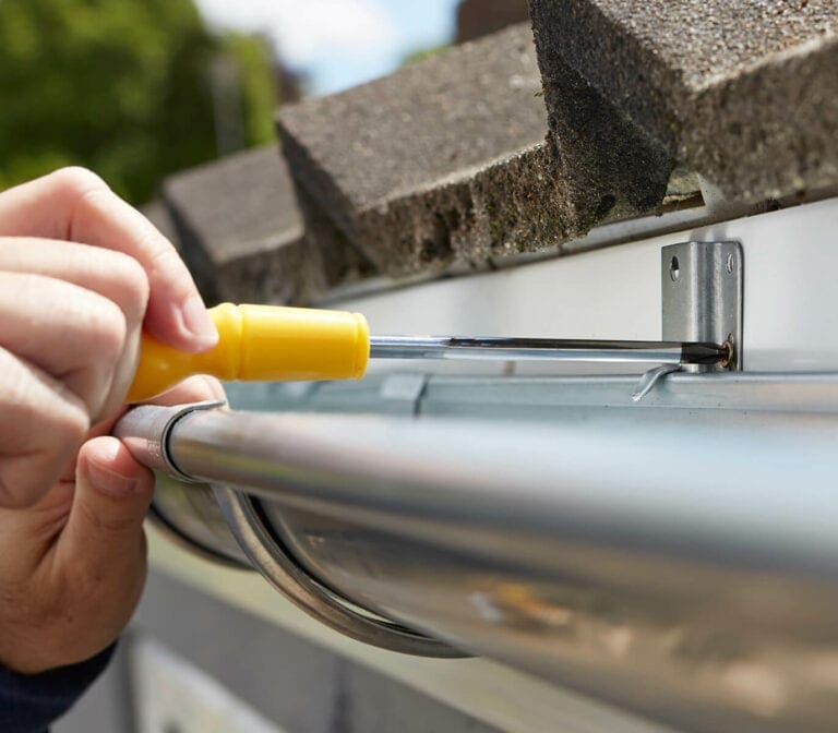 Installer fastening a half-round aluminum gutter below the roof edge