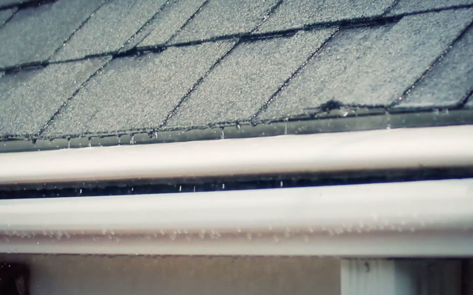 White seamless gutter along a shingle roof edge after a rain