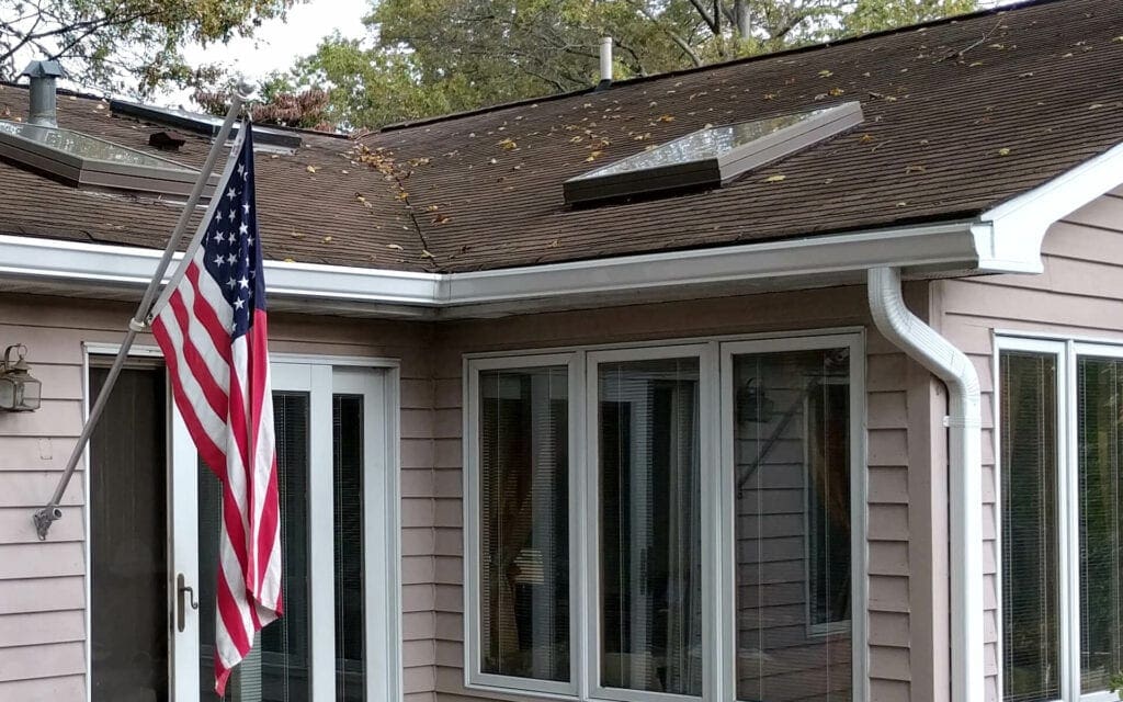 Home with white seamless gutters and downspouts and an American flag by the back door
