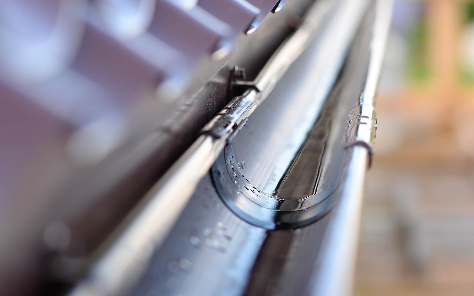 Close-up of a dark half-round gutter and its hanger brackets along a roof edge