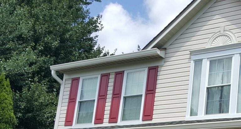 White K-style seamless gutter along the roofline of a beige house with red shutters