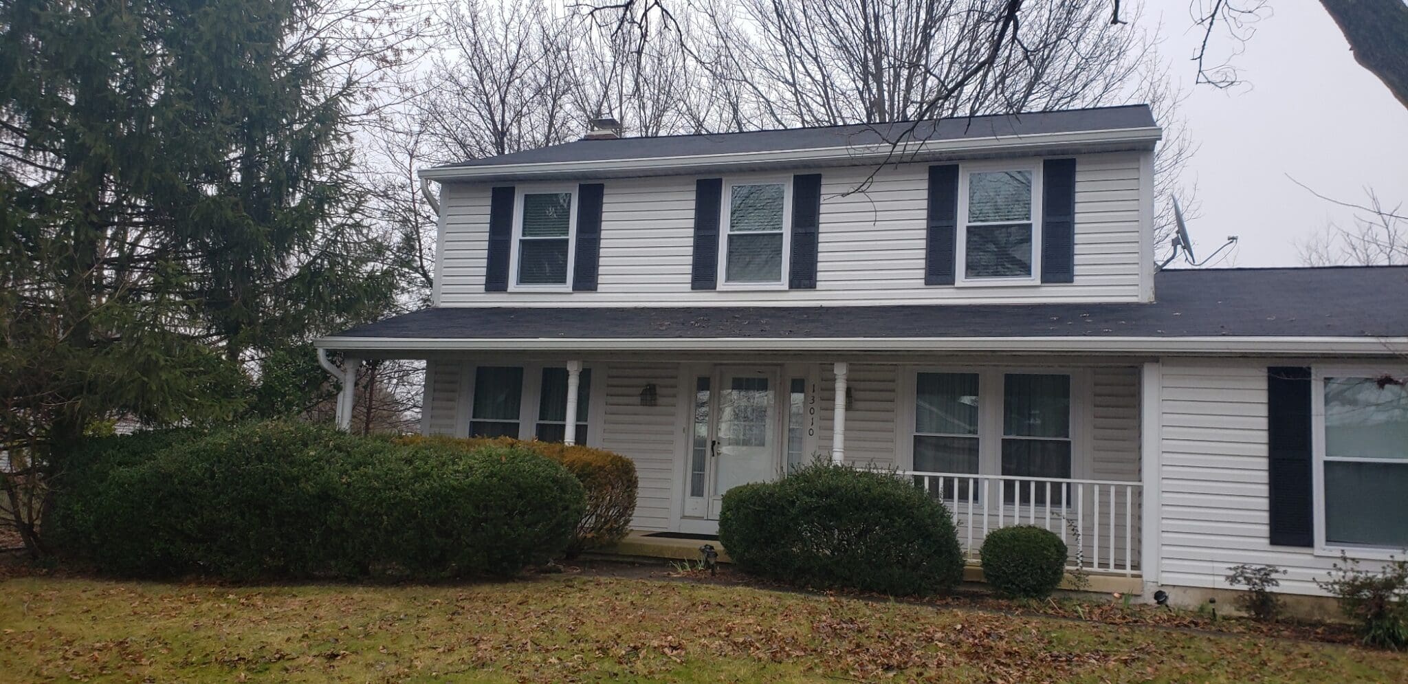 White two-story colonial with black shutters, a front porch and white gutters