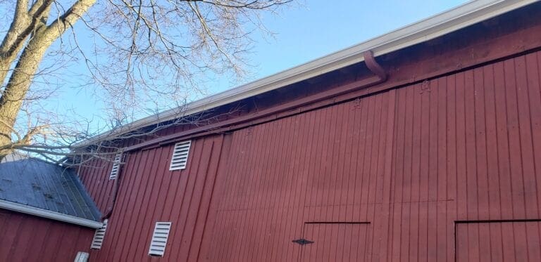 Red board-and-batten barn with a new white gutter and a red downspout