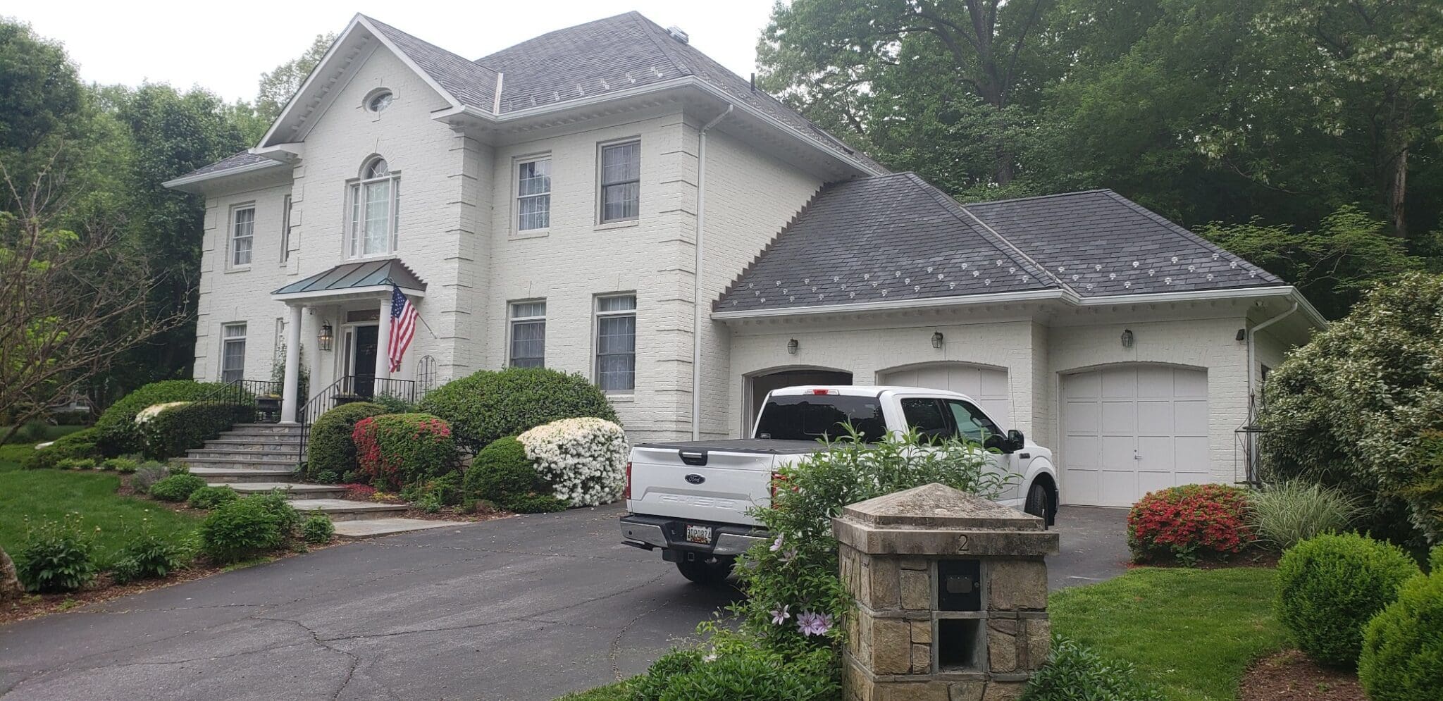 Large white colonial with a three-car garage, an American flag and a landscaped front yard