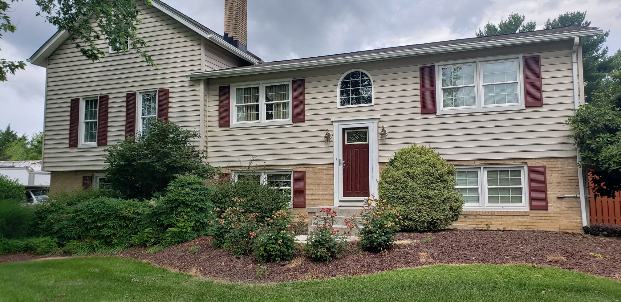 Tan split-level home with red shutters, a red front door and white gutters