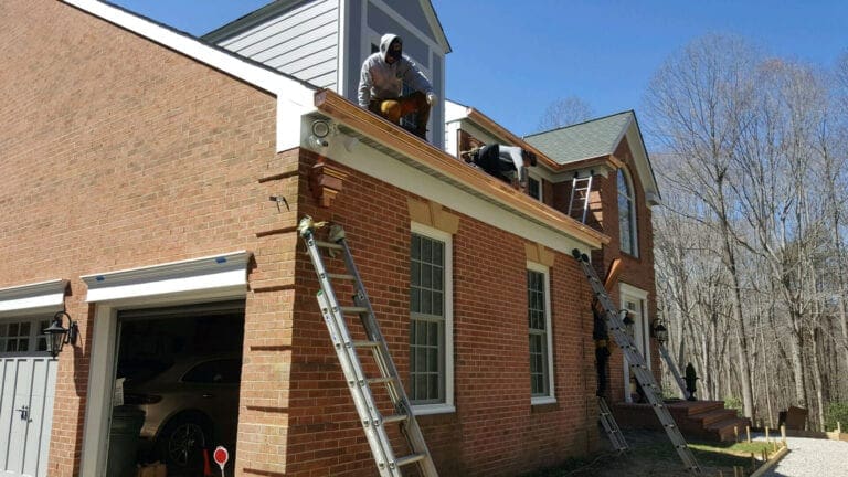 Crew installing copper gutters on a brick house with a ladder at the garage