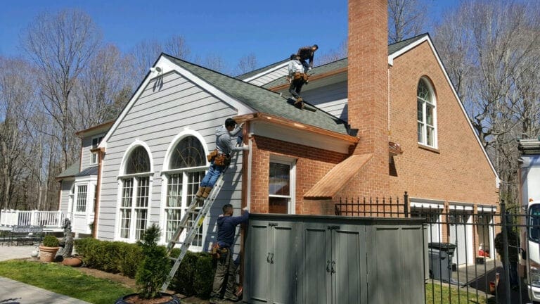 Crew on the roof and a ladder installing copper gutters on a brick and gray-sided home