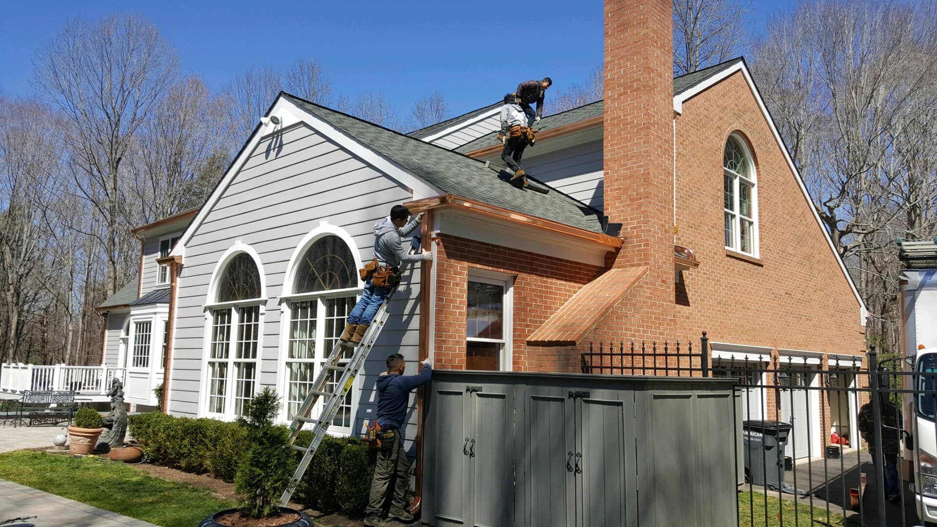 Next Day Gutters crew installing copper gutters on a brick and gray-sided home