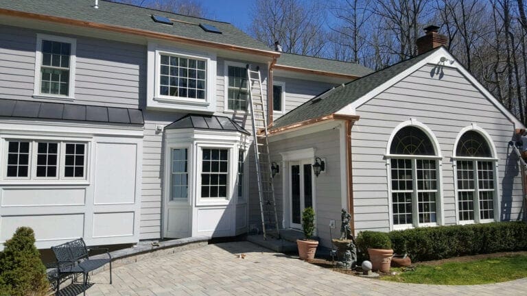 Back of a gray home with copper gutters above arched windows