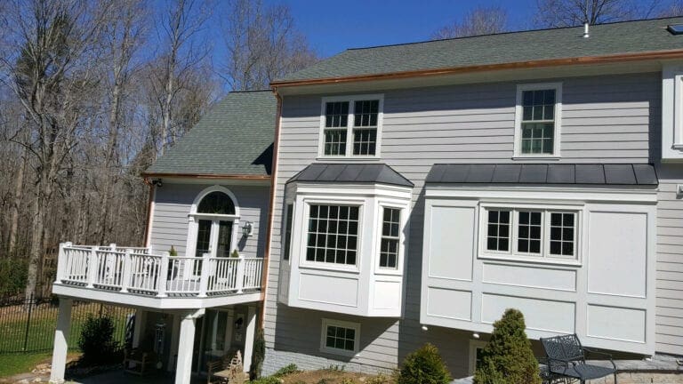 Gray-sided home with new copper gutters along the roofline above a white deck