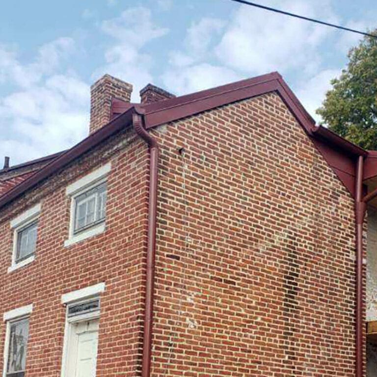 Historic brick house with dark red half-round gutters and a round downspout