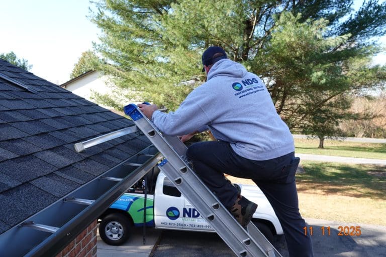 Next Day Gutters installer climbing a ladder to the roof, with a company truck in the driveway