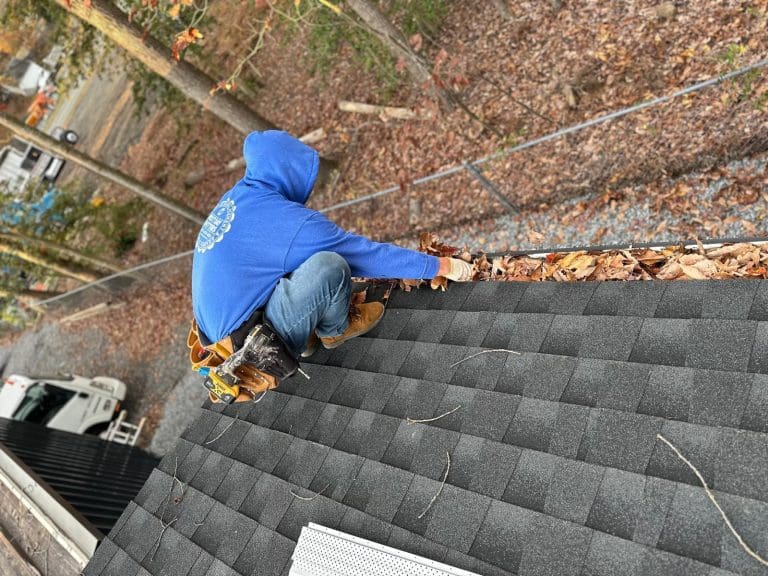 Next Day Gutters installer working along a leaf-filled gutter on a shingle roof