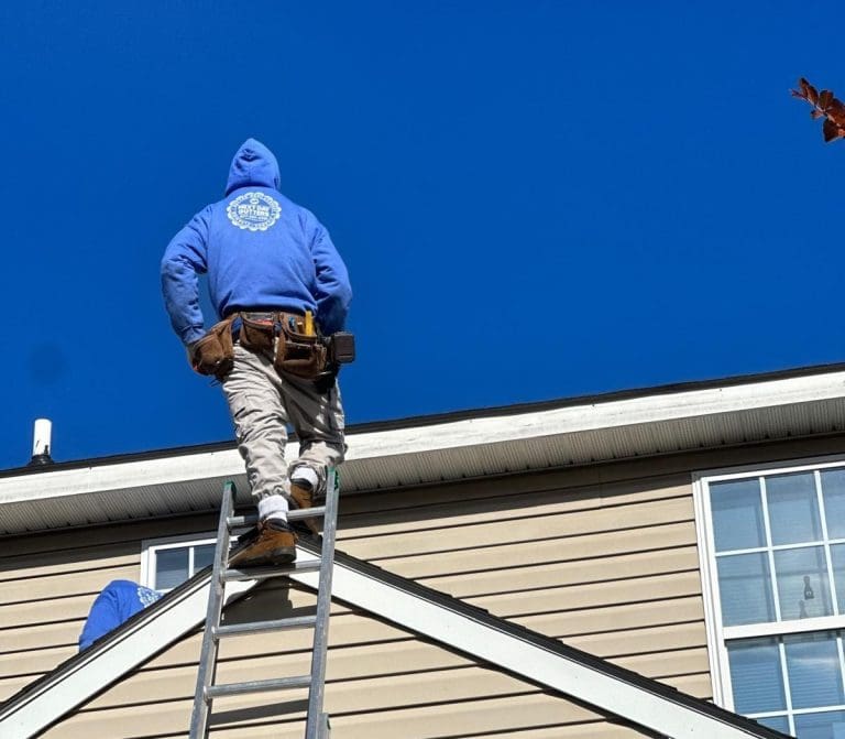 Next Day Gutters installer climbing a ladder to the roofline of a two-story home
