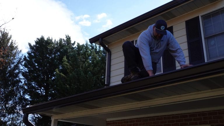 Next Day Gutters installer on a ladder at the roofline of a brick house