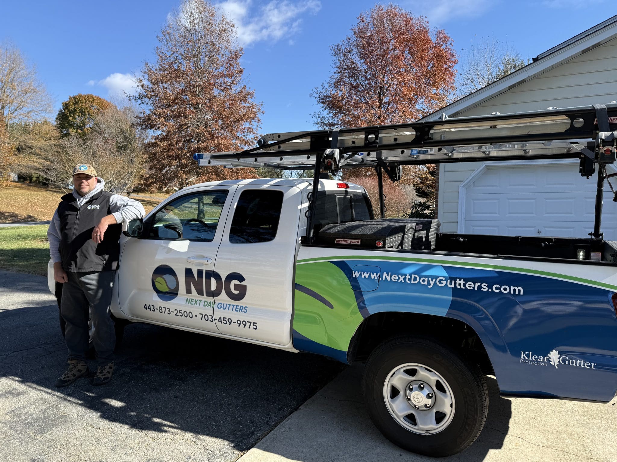 Next Day Gutters installer standing beside a company pickup truck with ladders on the rack
