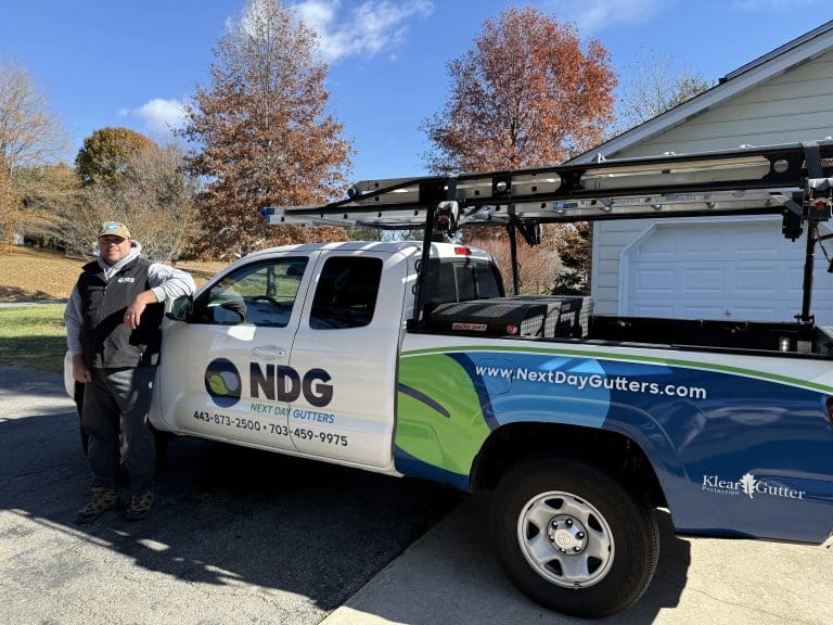 Next Day Gutters installer standing beside a company pickup truck with ladders on the rack
