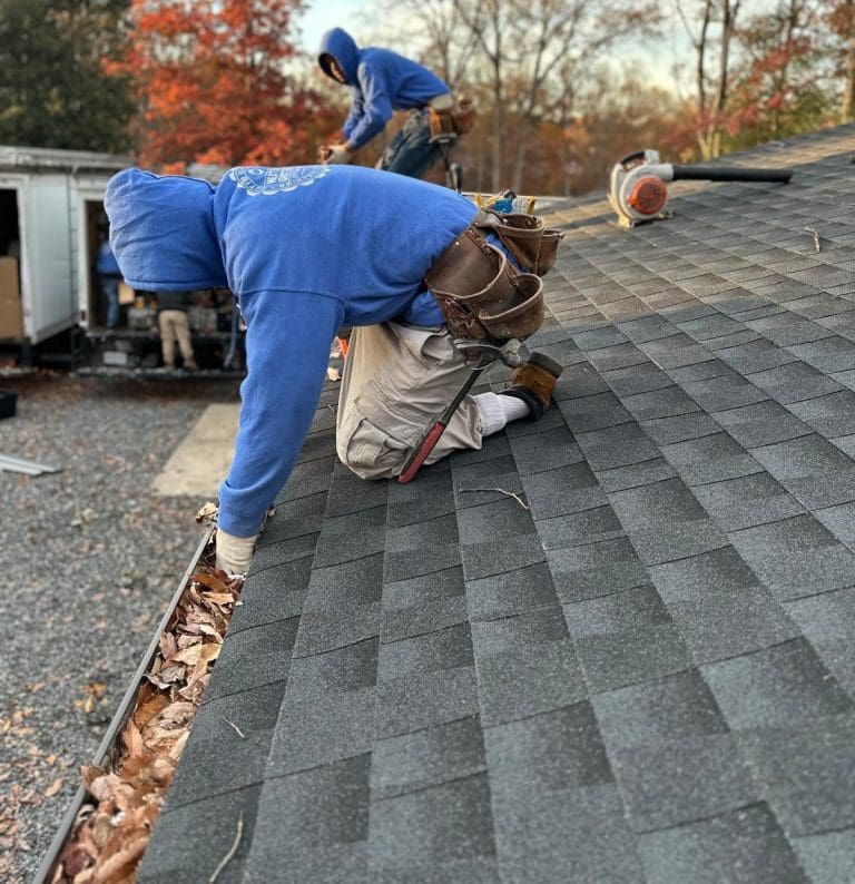 Next Day Gutters installer kneeling on a shingle roof at the gutter line