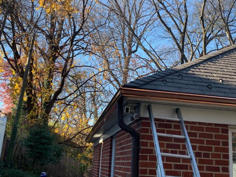 Copper K-style gutter on the corner of a brick house, ladder against the wall